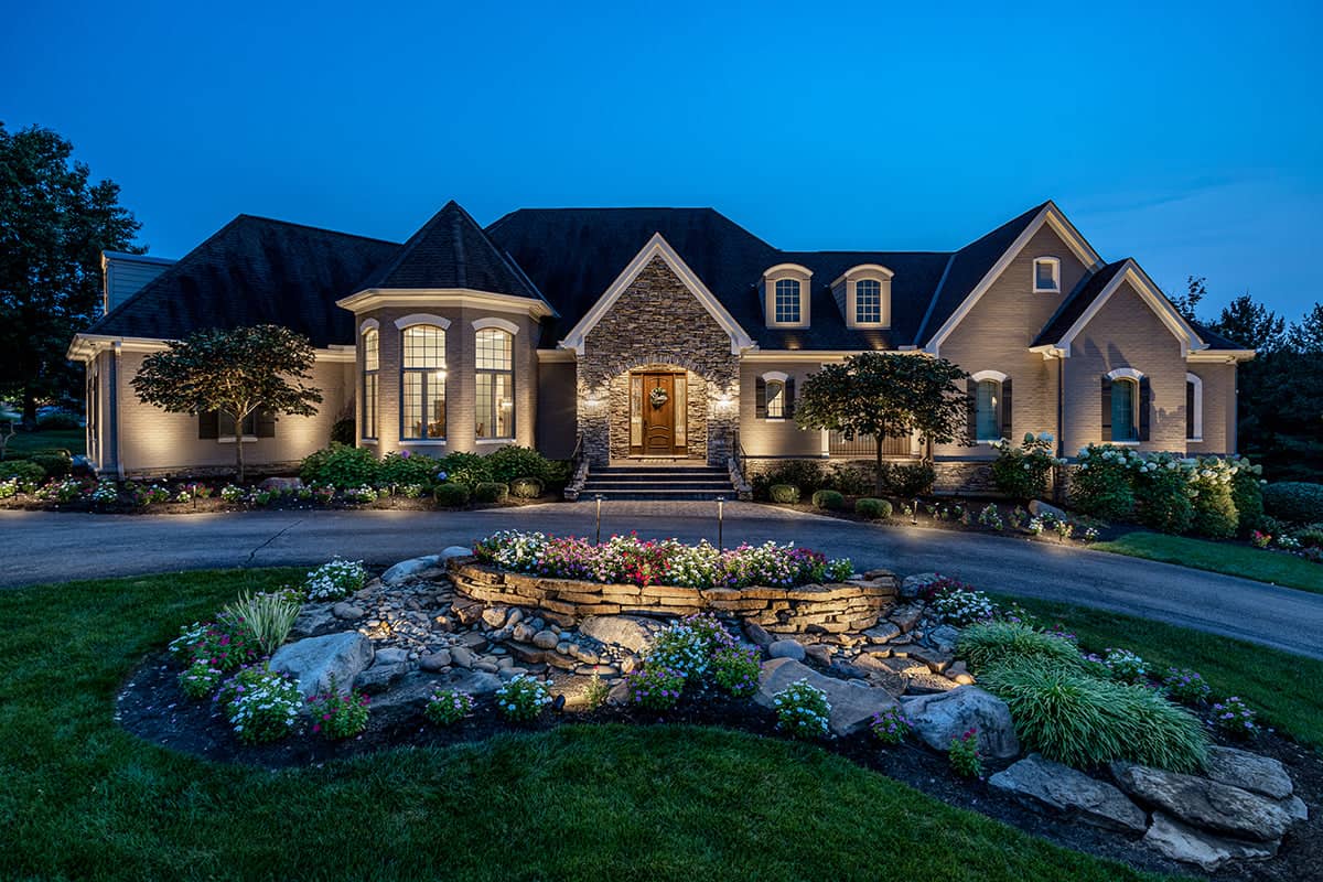 Elegant home with warm white outdoor lighting highlighting the landscape and facade at dusk.
