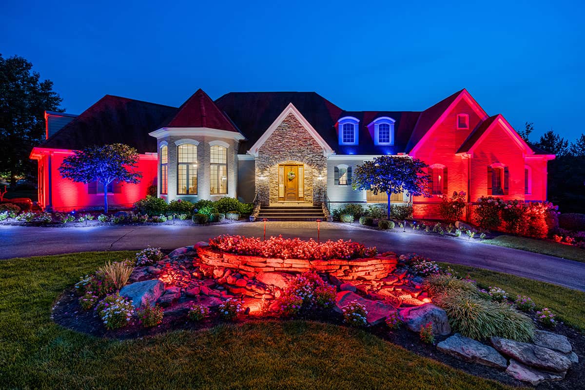 Elegant home illuminated with red, white, and blue outdoor lighting at dusk.