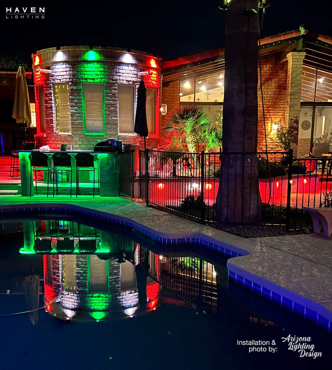 Poolside patio with vibrant red, green, and white lighting reflecting on the water at night.