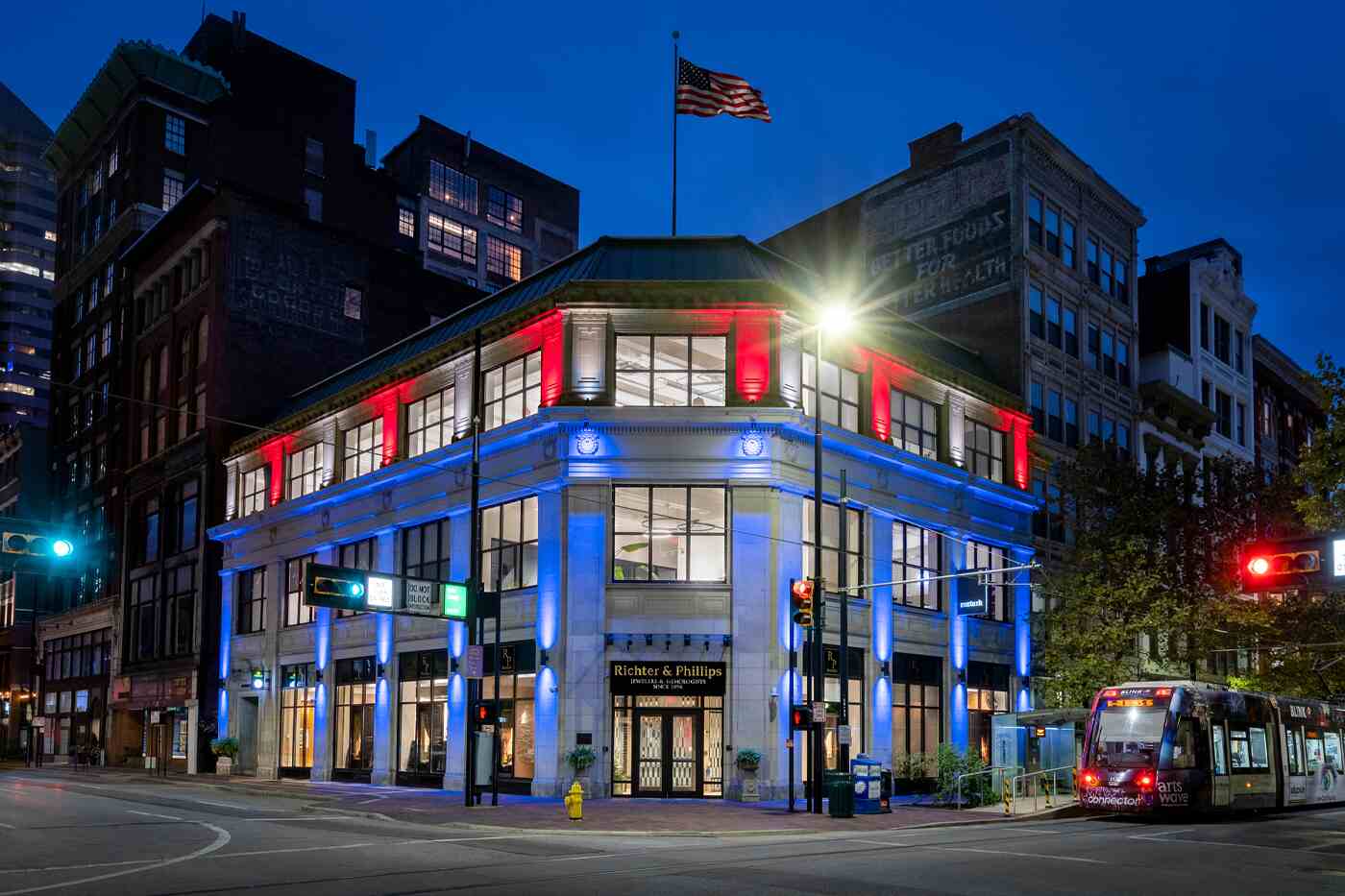 Downtown building at night illuminated with vibrant red, white, and blue 9 Series Pro Full Color LED lights, highlighting its architecture, with an American flag on the roof and a passing streetcar.