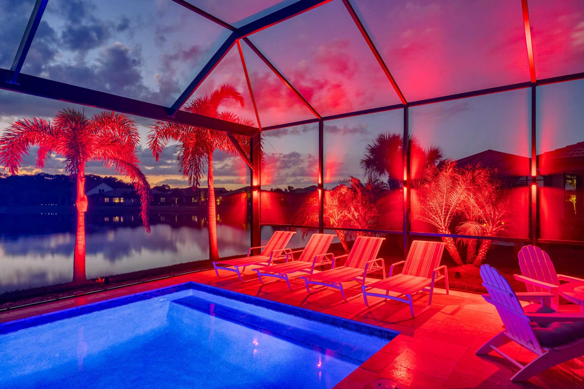 Screened-in pool area with bold red lighting and a sunset lake view.