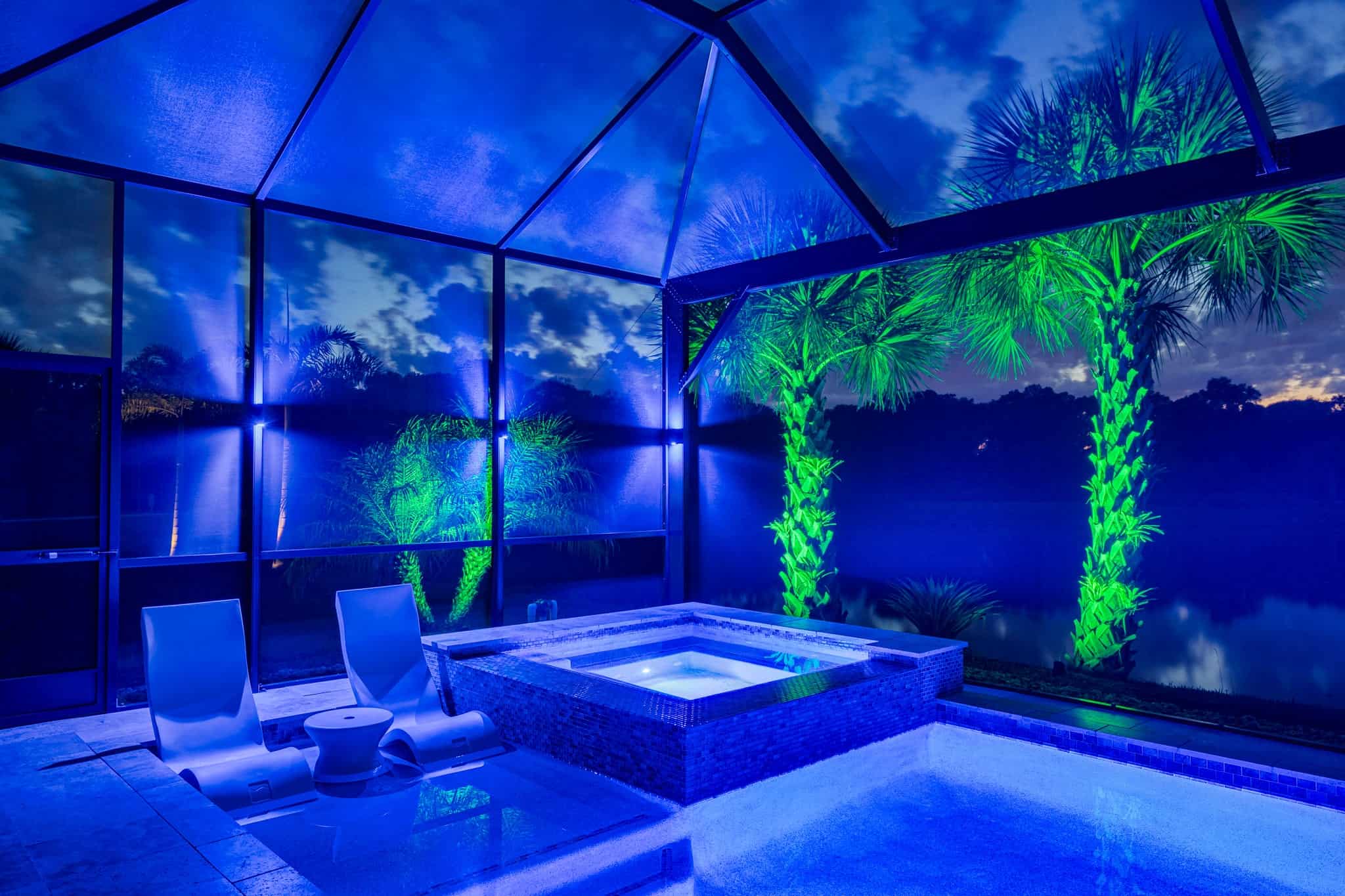 Screened-in pool with vibrant blue and green lighting at night.