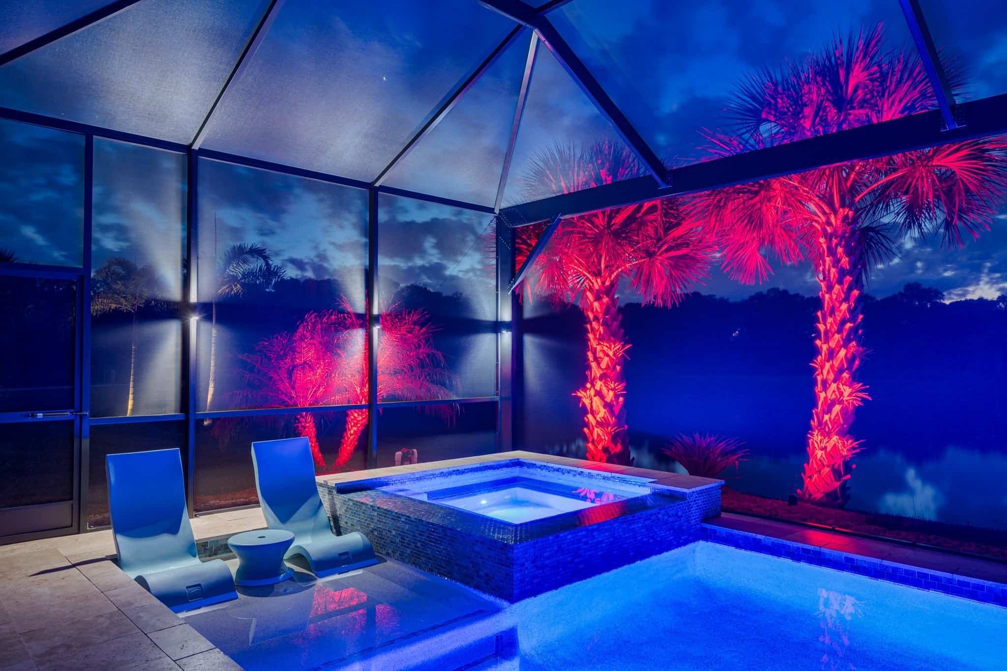 Screened-in pool with vibrant red and blue lighting at night.