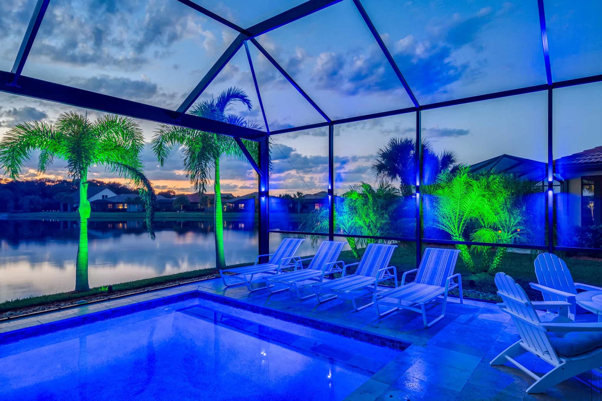 Enclosed poolside patio with blue and green outdoor lighting at sunset.