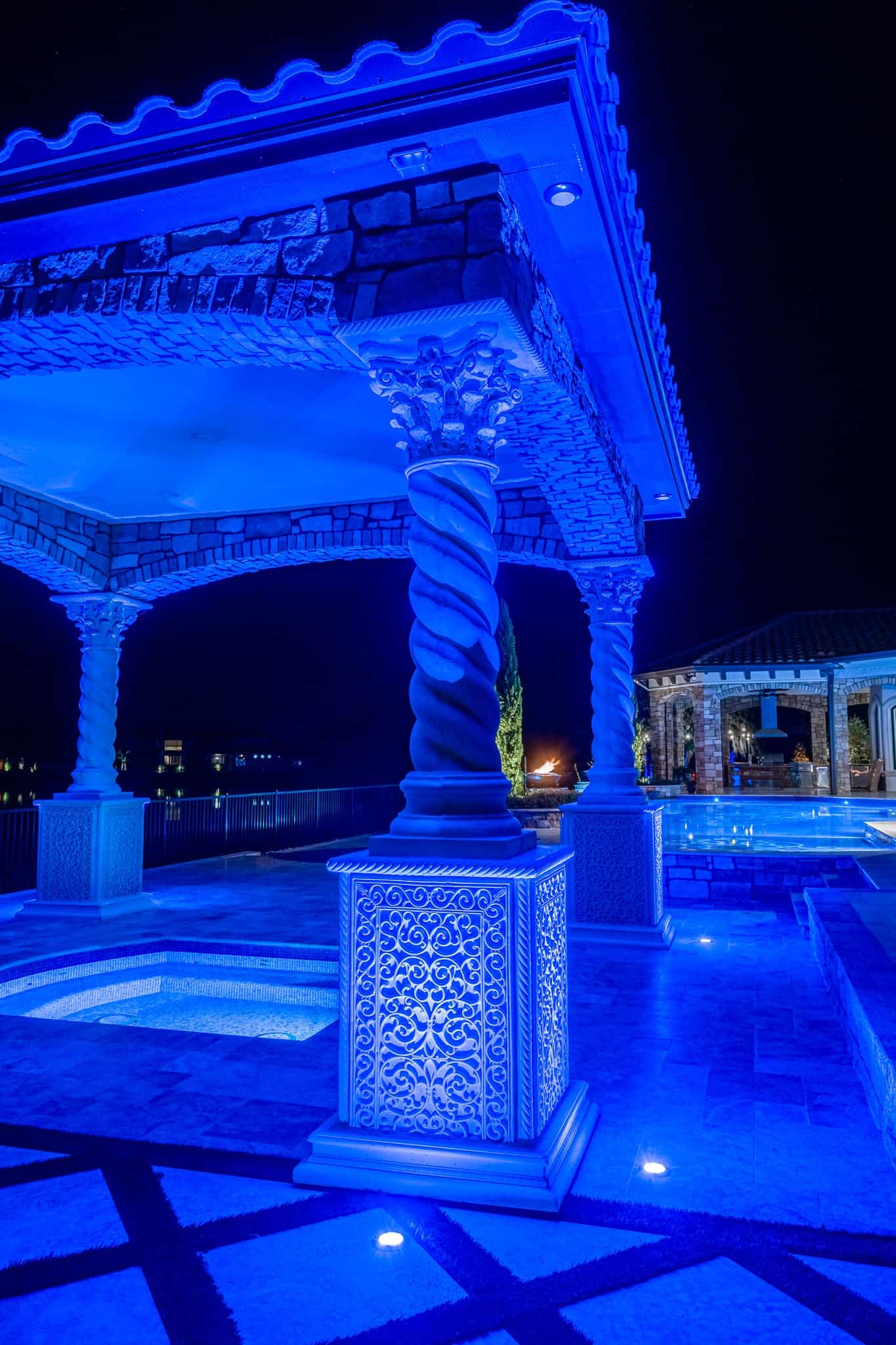 Ornate poolside pavilion illuminated with vibrant blue lighting at night.
