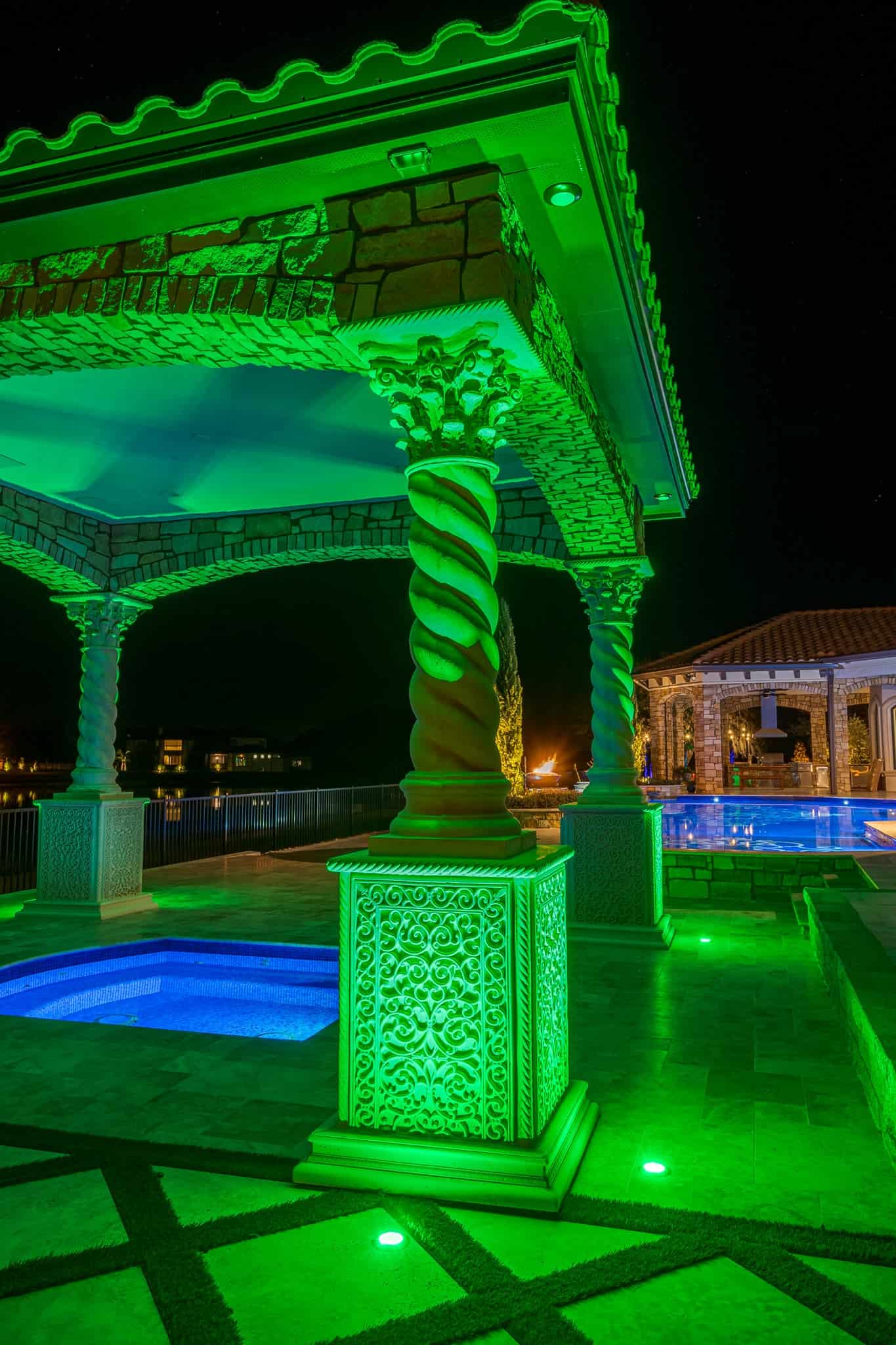 Ornate poolside pavilion illuminated with vibrant green lighting at night.