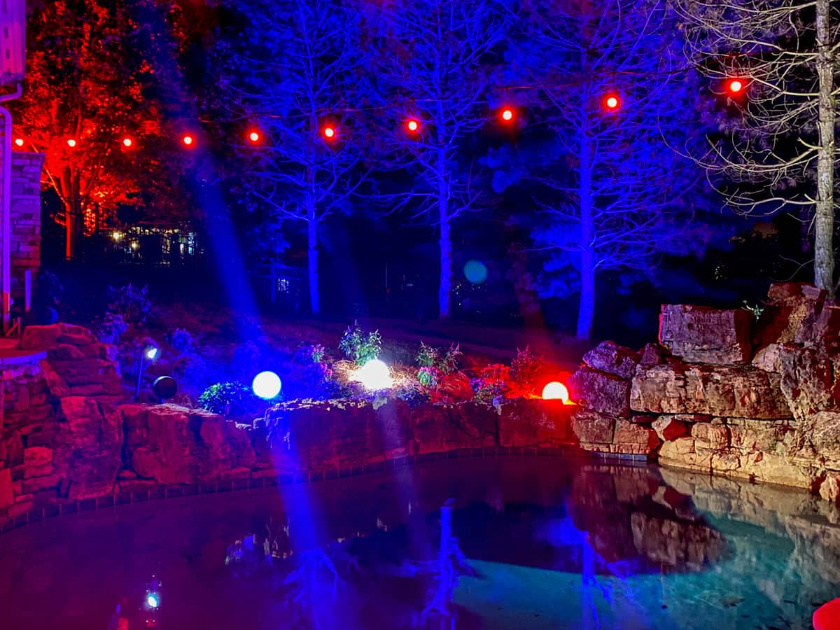 Poolside landscape illuminated with vibrant red, white, and blue lighting at night.