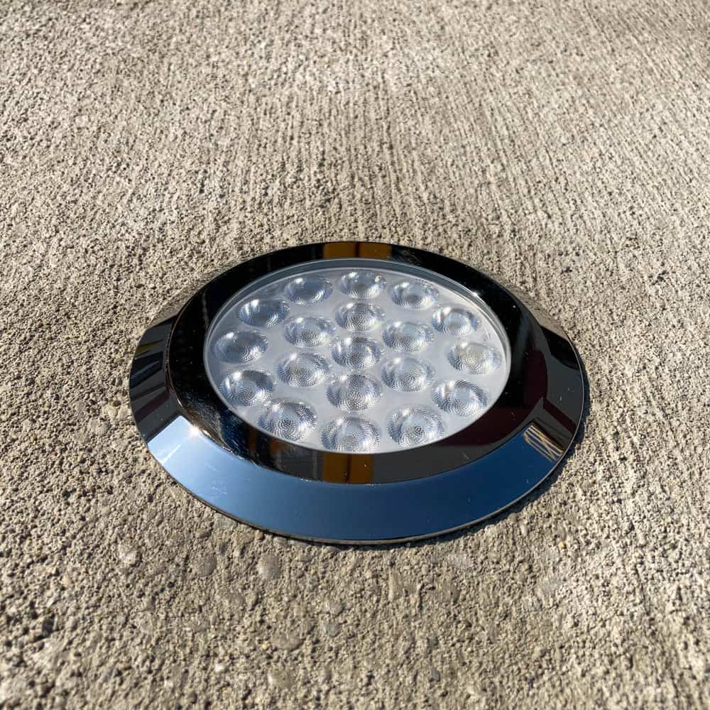 In-ground LED light with a chrome finish installed on a concrete surface.