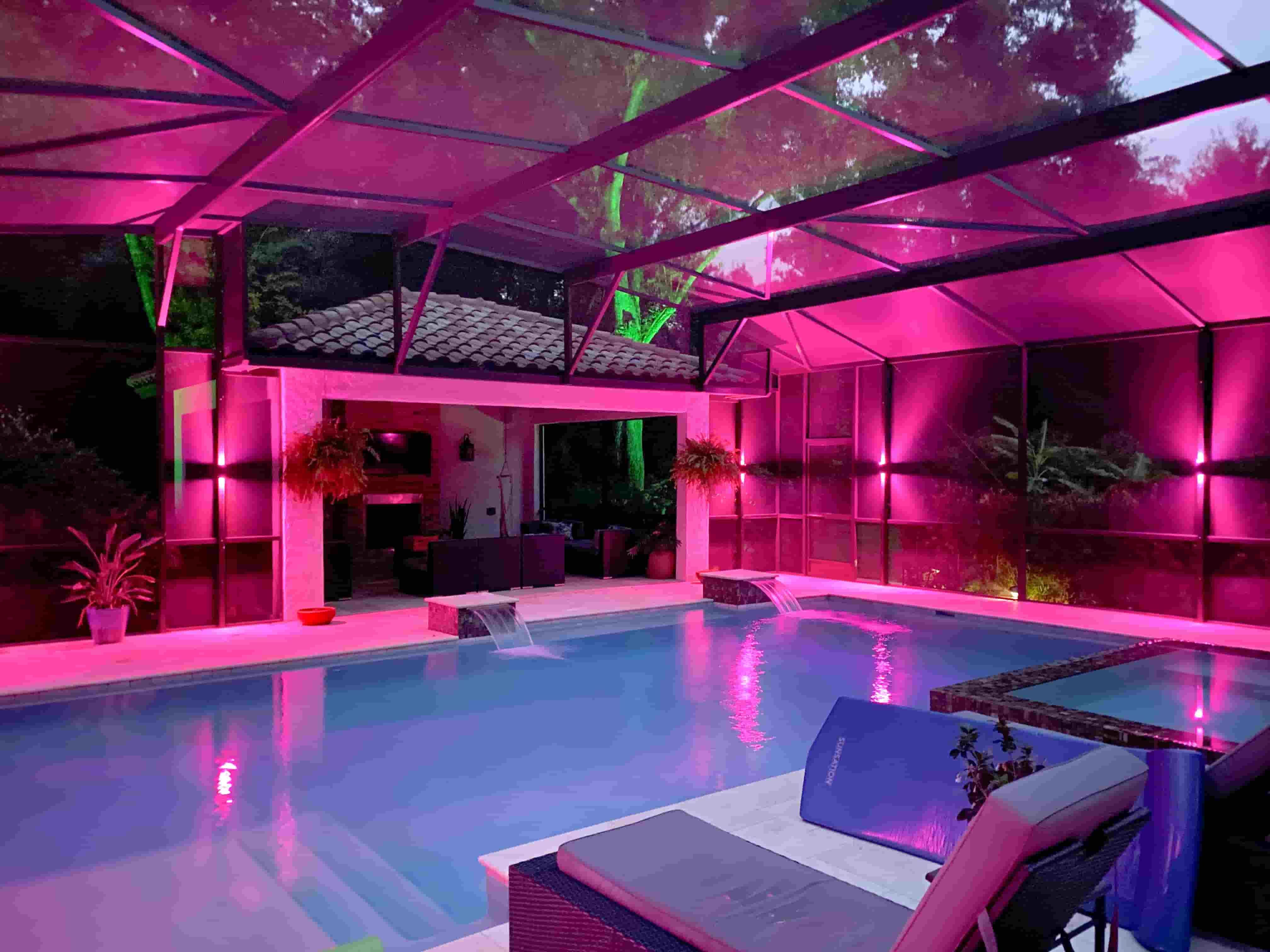 Luxury pool area with vibrant pink and green LED enclosure lighting,