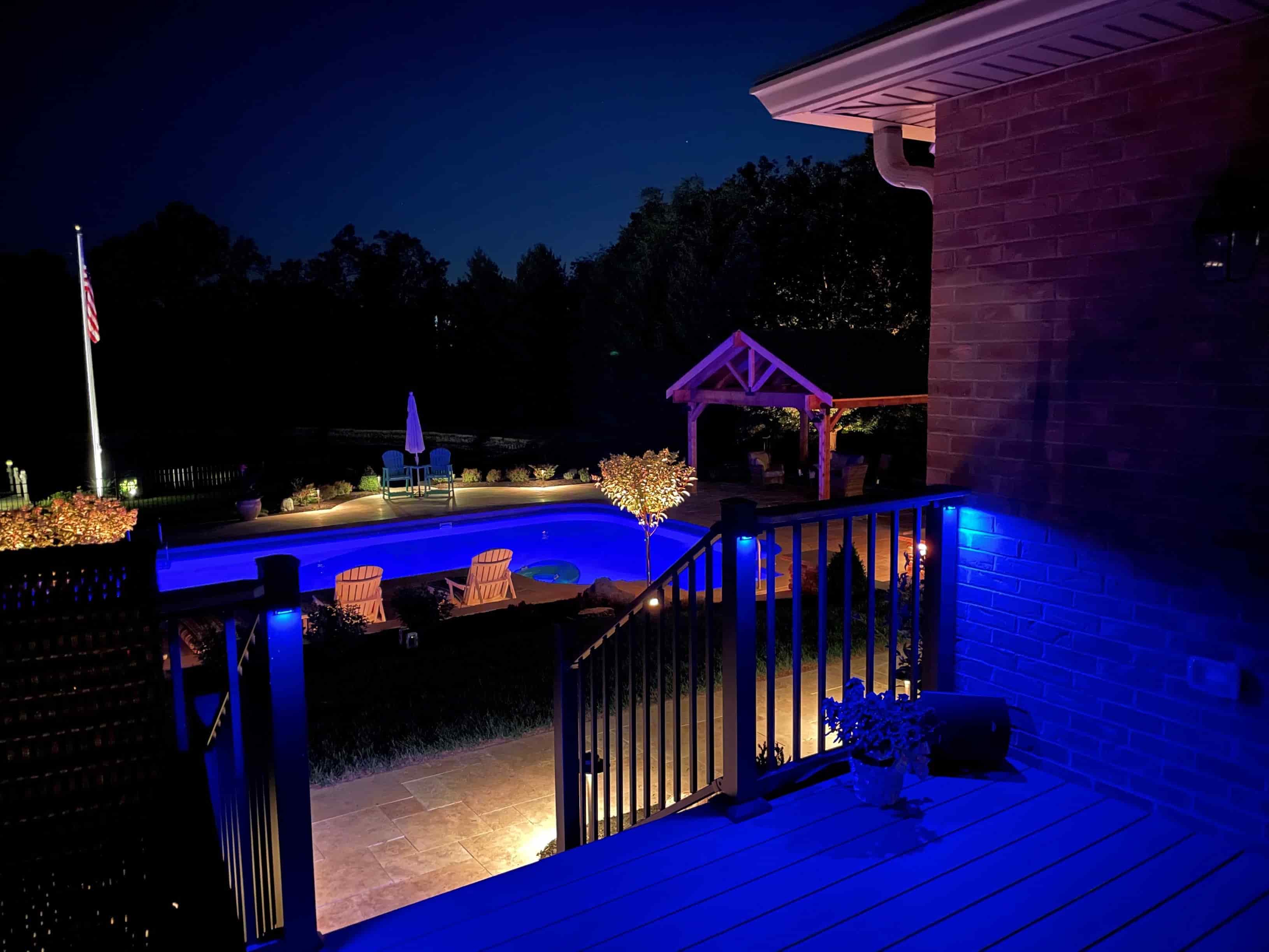 Outdoor poolside deck illuminated with blue accent lighting at night.