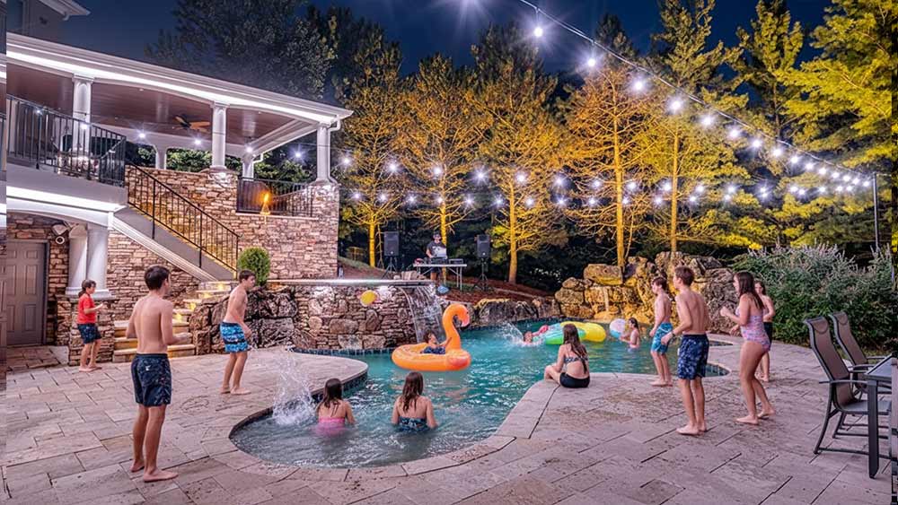 Backyard lit up with Haven Lighting and kids playing in a pool