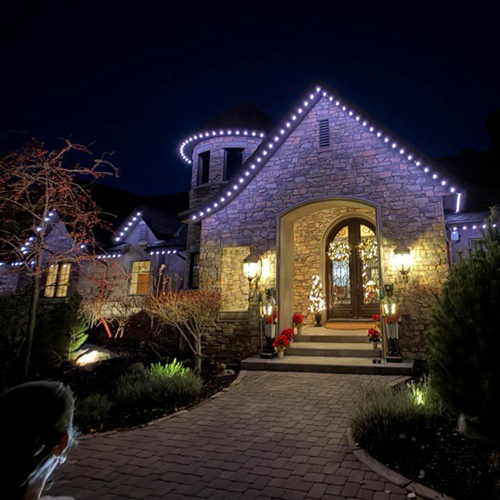 Home with classic permanent roofline lighting and landscape accent lighting at night